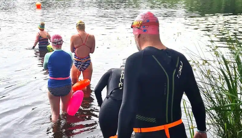 Swimmers in wetsuits with tow floats and swimming caps starting a swim in Knutsford Mere