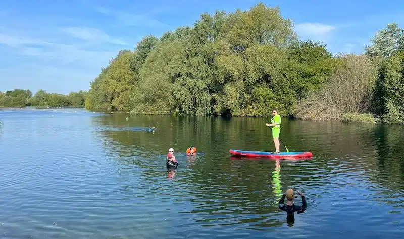 Swimmers and a man on a canoe enjoying Redricks Lake in Hertfordshire