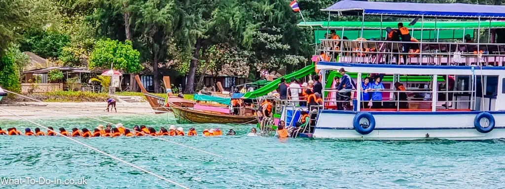 A line of tourists disembarking a ferry and walking in the sea at Koh Kradan, Thailand