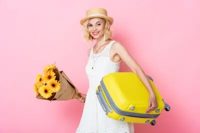 young woman in straw hat holding flowers and luggage